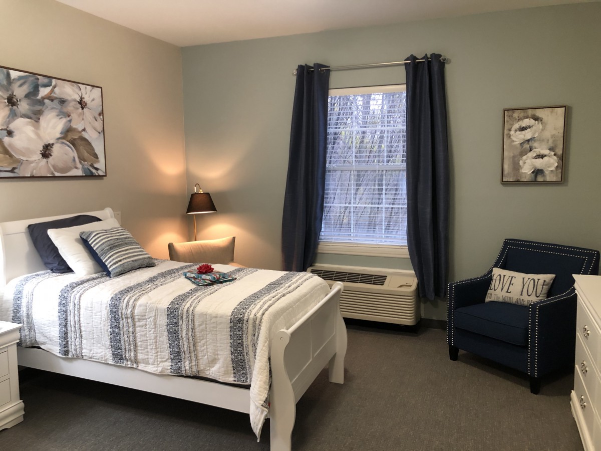 A cozy bedroom with a neatly made bed, accented by a lamp and dark curtains.