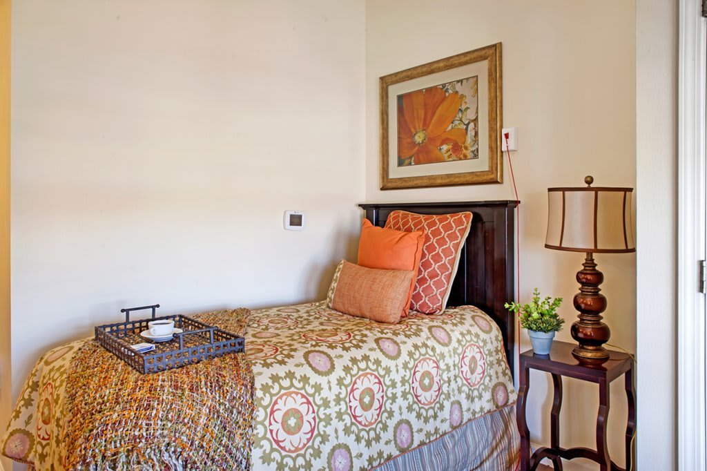 A cozy bedroom setup with a single bed adorned with decorative pillows, wall art, and a bedside lamp.