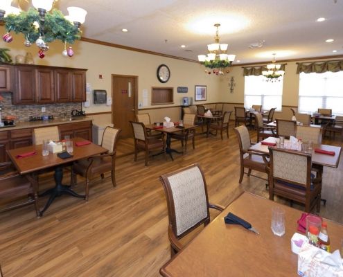 An elegantly furnished dining room with tables and chairs, featuring warm wood flooring and decorative chandeliers.
