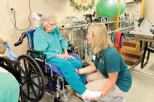 A healthcare professional assisting an elderly patient in a wheelchair during a physical therapy session.