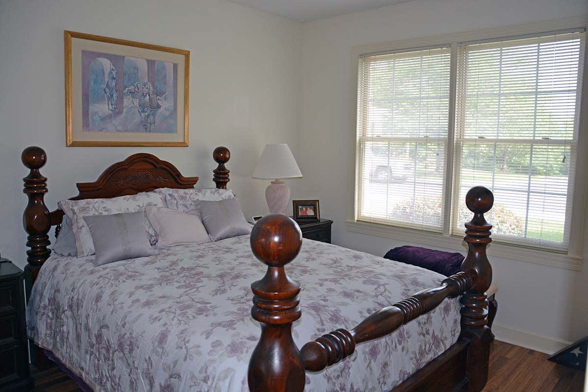 A cozy bedroom with a wooden bed frame and soft bedding, featuring a window and a side lamp.