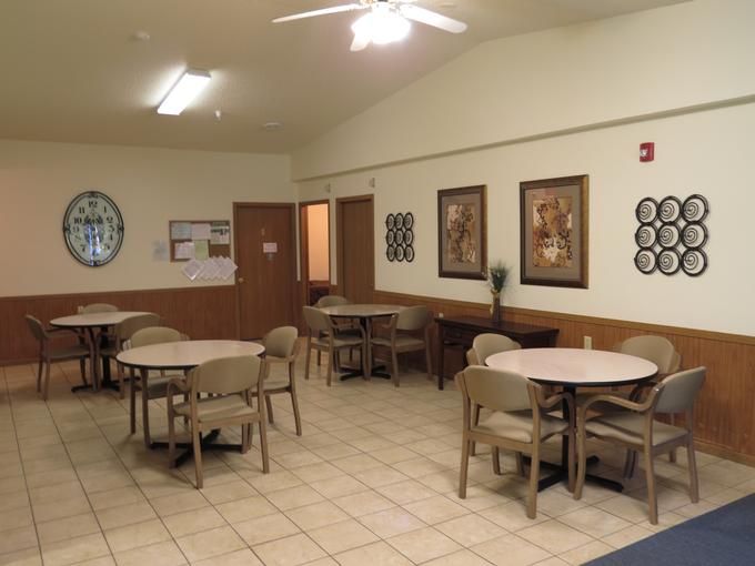 An empty room with several tables and chairs, featuring wall decorations and a tile floor.