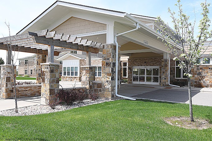 A modern building with a stone facade and a covered entrance surrounded by green grass.