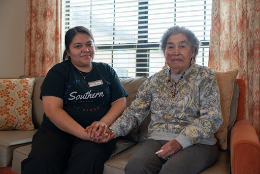 A caregiver and an elderly woman share a moment of companionship while sitting together.