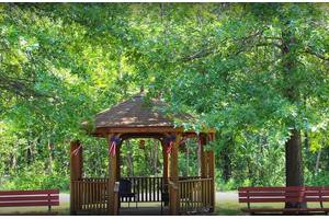 A serene park setting with a charming wooden gazebo surrounded by lush greenery and benches.