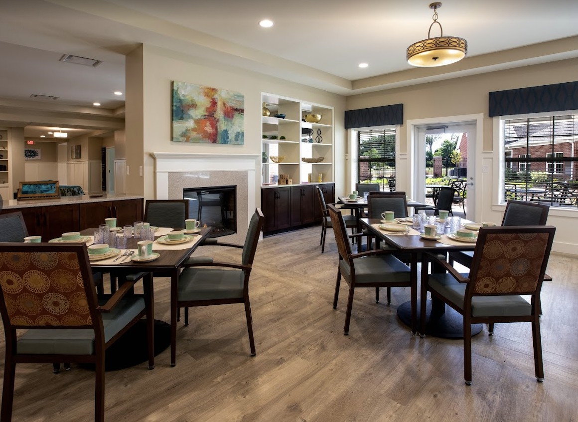 A cozy dining area featuring elegant tables and chairs, with a fireplace and artwork adding warmth to the space.