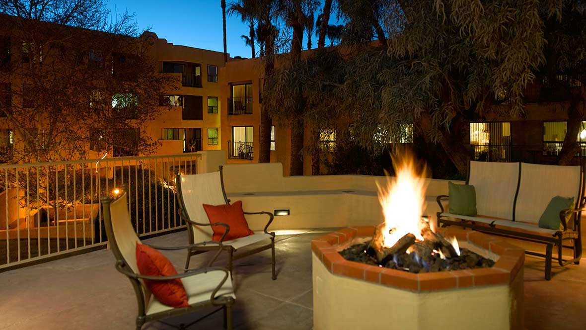 A cozy outdoor patio with a fire pit and seating at night, adjacent to an apartment building.
