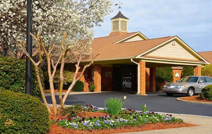 A landscaped entrance to a brick building with a driveway and floral arrangements.
