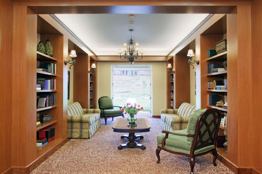 A cozy library space featuring plush seating and well-stocked bookshelves, illuminated by a decorative chandelier.