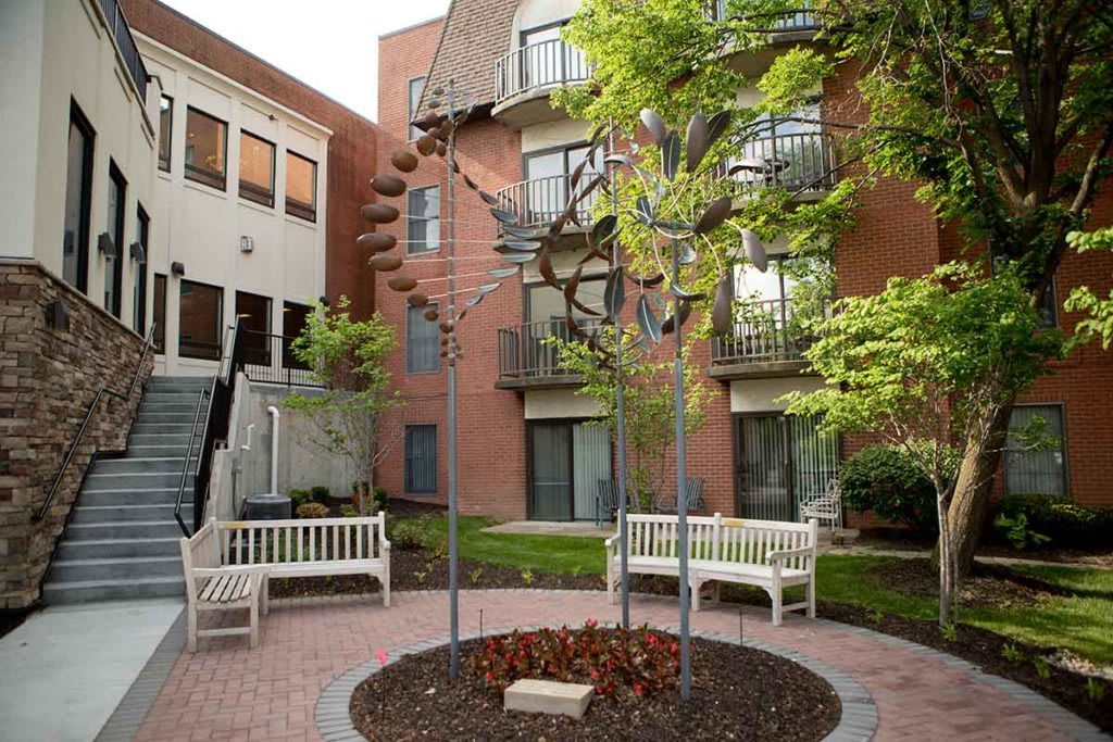 A serene courtyard featuring a modern art sculpture surrounded by benches and greenery.