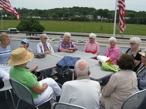 A group of senior citizens enjoying a sunny day together, engaged in conversation at a table outside.