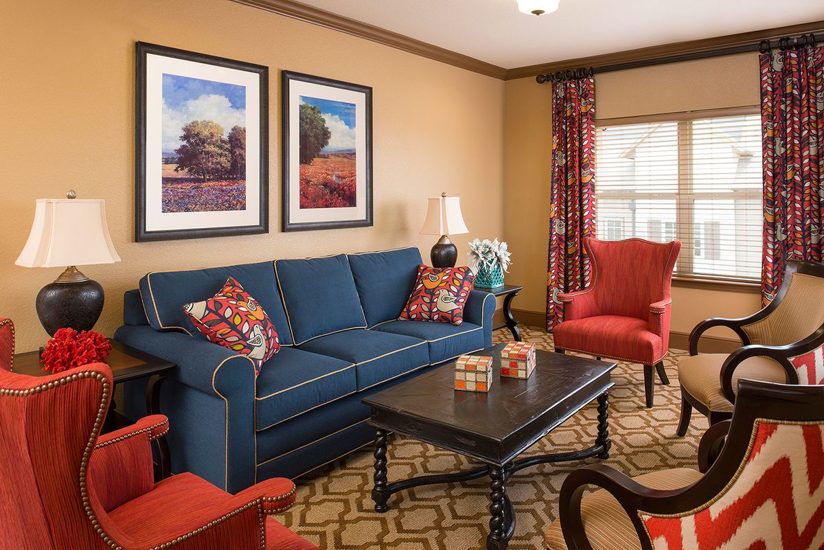 A cozy living room with a blue sofa, accented by red chairs and decorative pillows, featuring framed artwork and a stylish coffee table.
