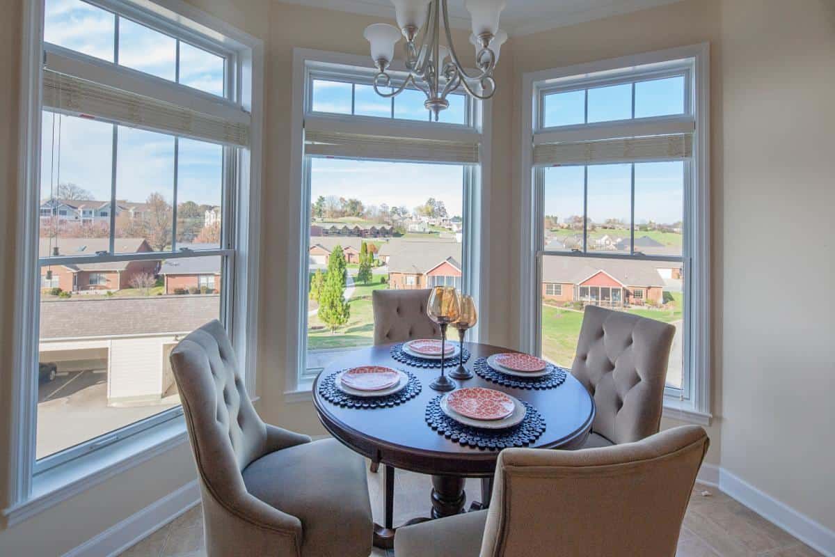 A cozy dining area with a round table set for four, surrounded by large windows that let in ample natural light.