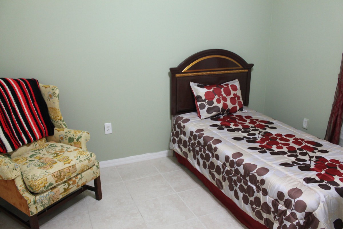 A small bedroom with a single bed and floral bedding, alongside a vintage chair and green walls.