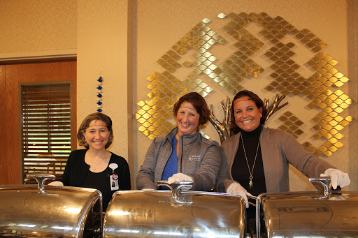 Three women smiling behind a catering setup.