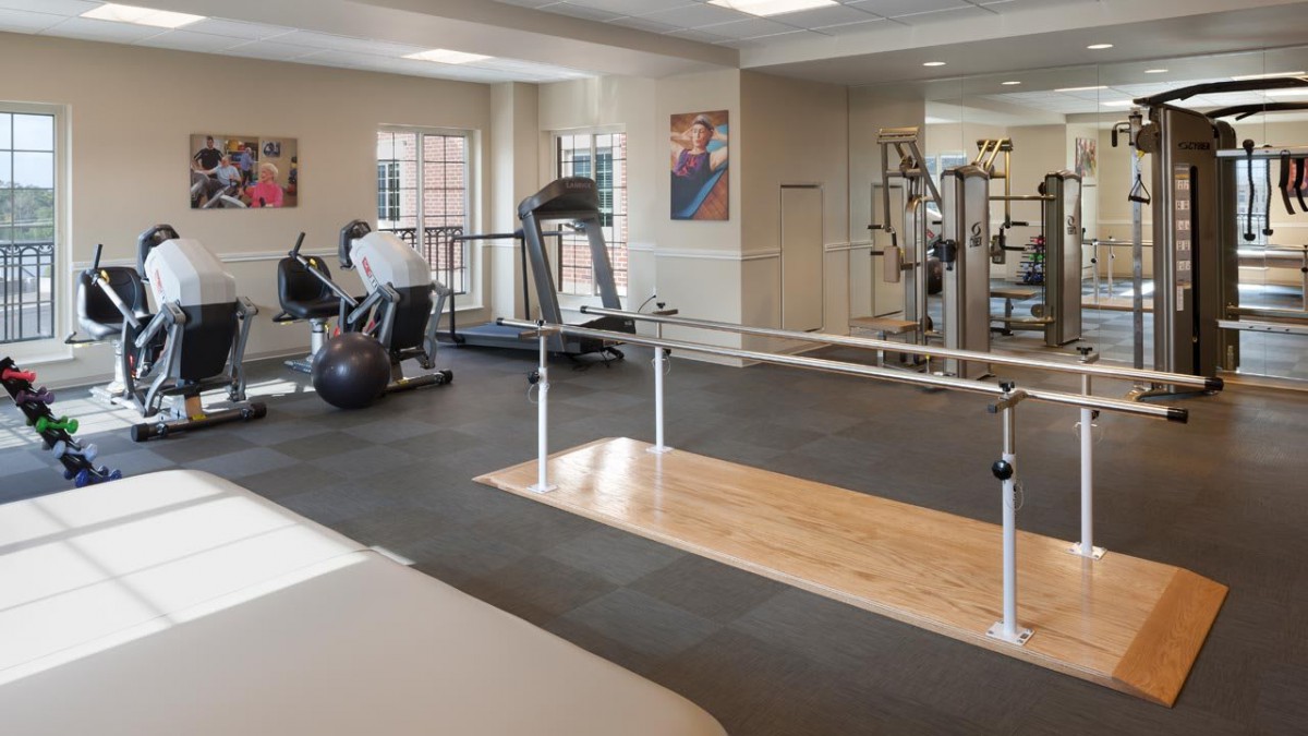A well-equipped indoor gym featuring various exercise machines and parallel bars for fitness and rehabilitation.