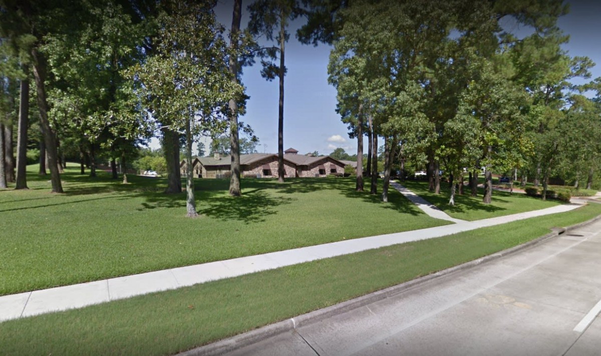 A suburban house surrounded by trees and a well-maintained lawn, with a sidewalk in the foreground.
