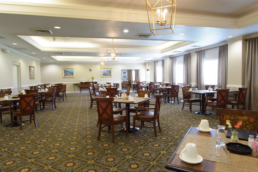An empty dining room with neatly arranged tables and chairs, featuring elegant lighting and a carpeted floor.
