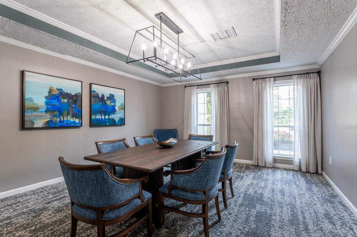 A beautifully designed dining room featuring a rectangular table surrounded by blue upholstered chairs, artwork on the walls, and a modern chandelier overhead.