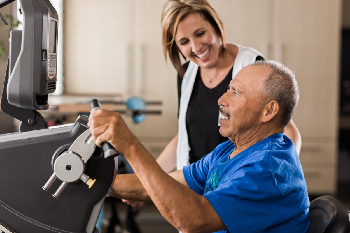 A healthcare professional assists an elderly man during a physical therapy session.