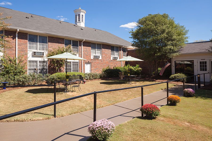 A quaint outdoor area with a brick building, surrounded by a garden and trees under a clear blue sky.
