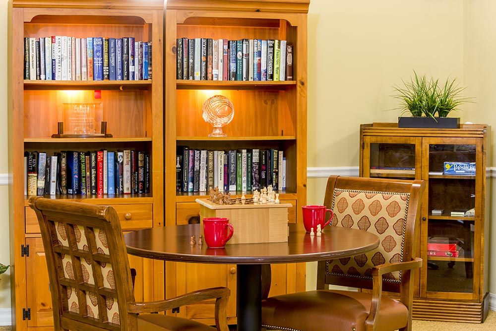 A cozy library setting with a wooden bookshelf, a round table, and chairs.