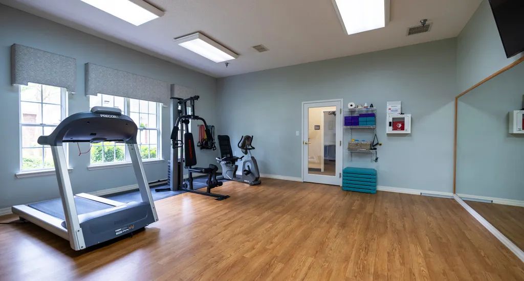 A clean and well-lit gym with exercise equipment including a treadmill and weights.
