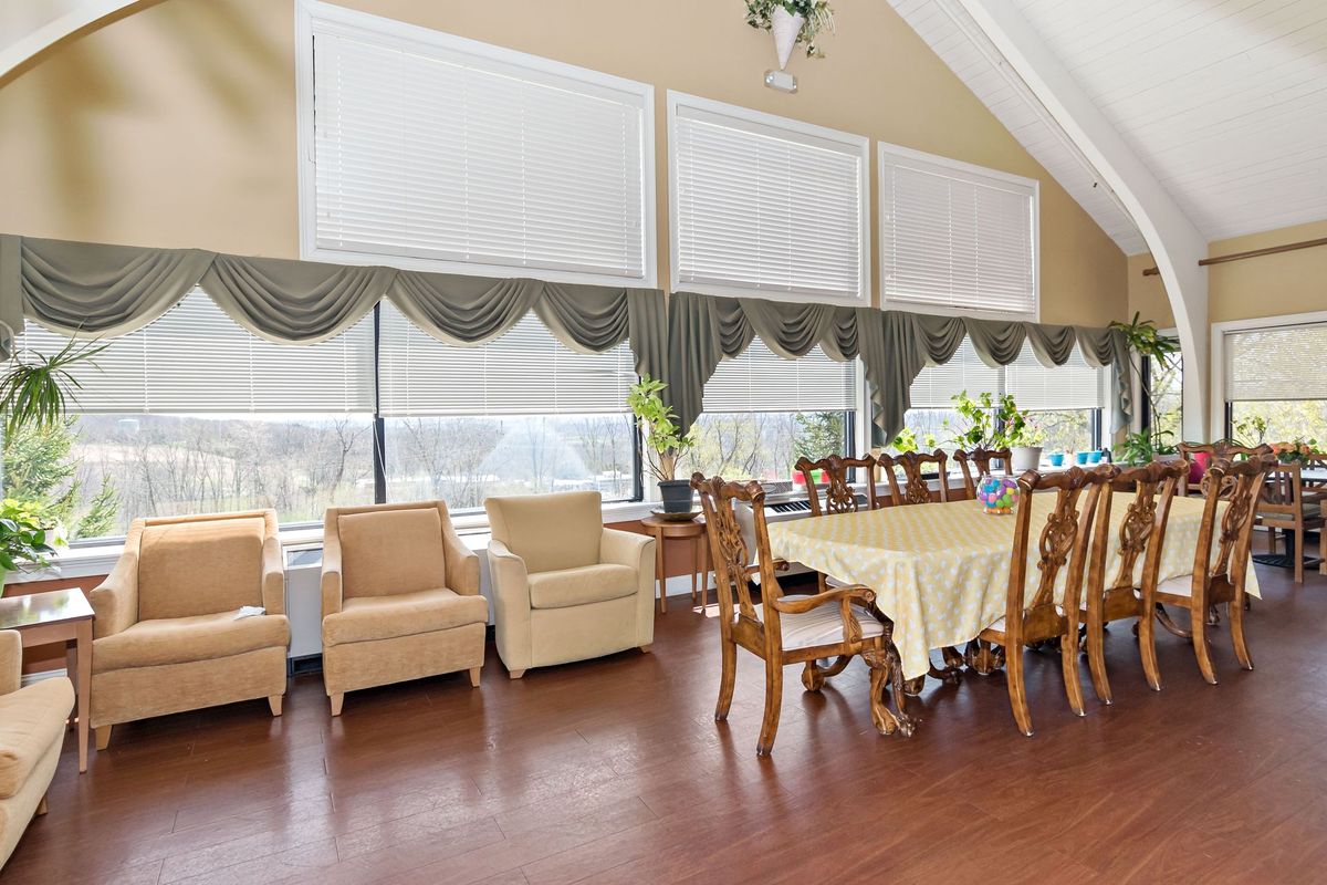 A spacious dining room with a long table, chairs, and large windows with curtains.