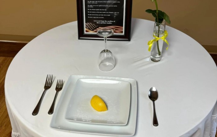 A symbolic table setting with a lemon slice, an inverted glass, and a single rose, representing remembrance for veterans.