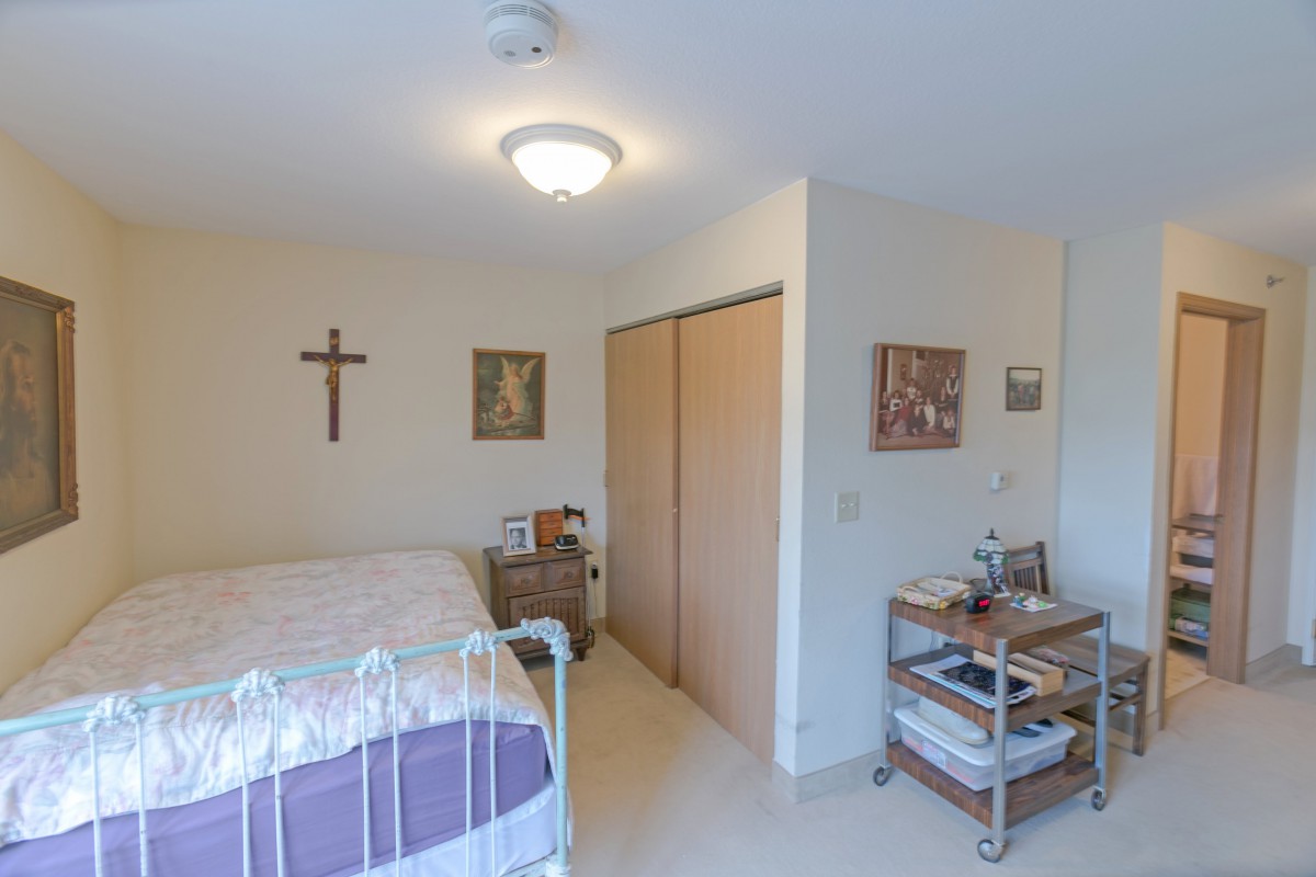 A simple bedroom with religious decorations, featuring a single bed and a small wooden nightstand.