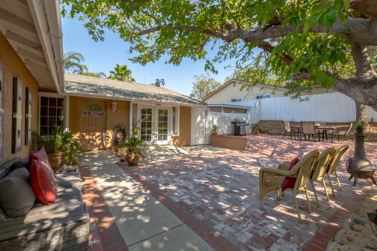 A sunny backyard with a spacious patio area, featuring outdoor seating and surrounded by trees.