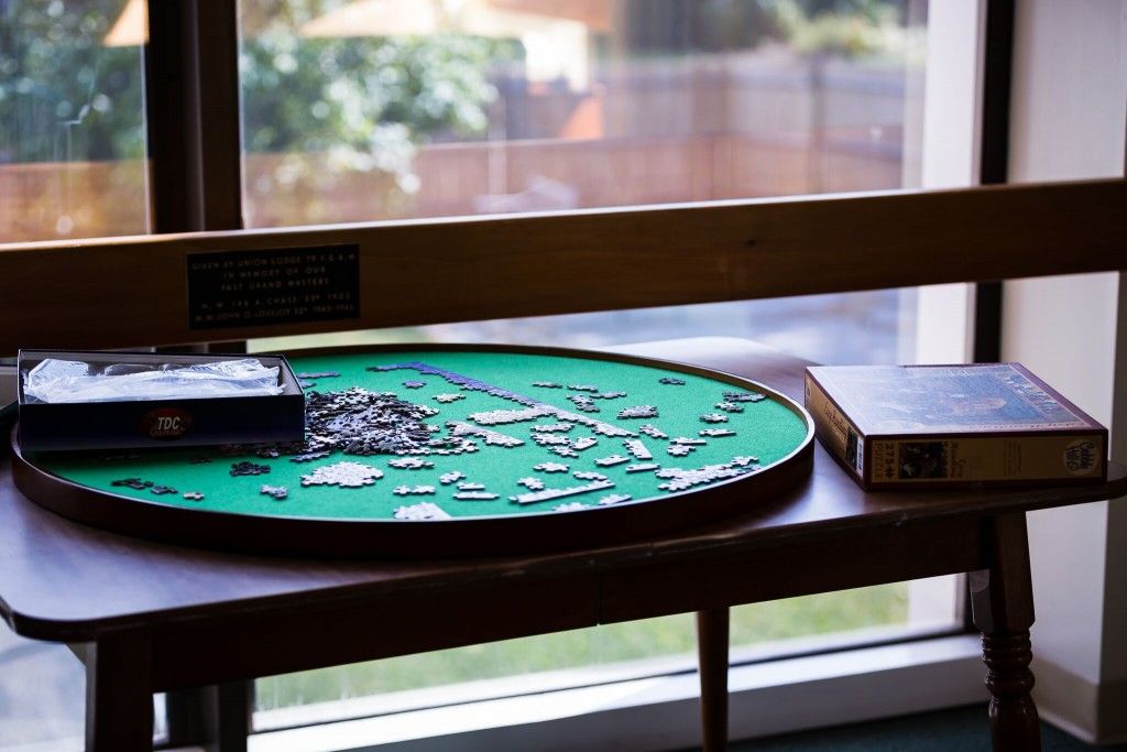 A partially completed jigsaw puzzle on a round table by the window.