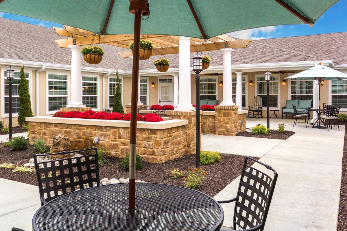 A peaceful outdoor patio area with tables, chairs, and a green umbrella set in a landscaped garden.