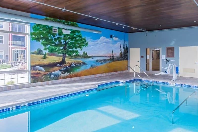 An indoor swimming pool with a vibrant mural of a scenic landscape on the wall.