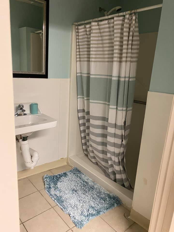 A bathroom with a shower and curtain, sink with a mirror, and a blue rug.