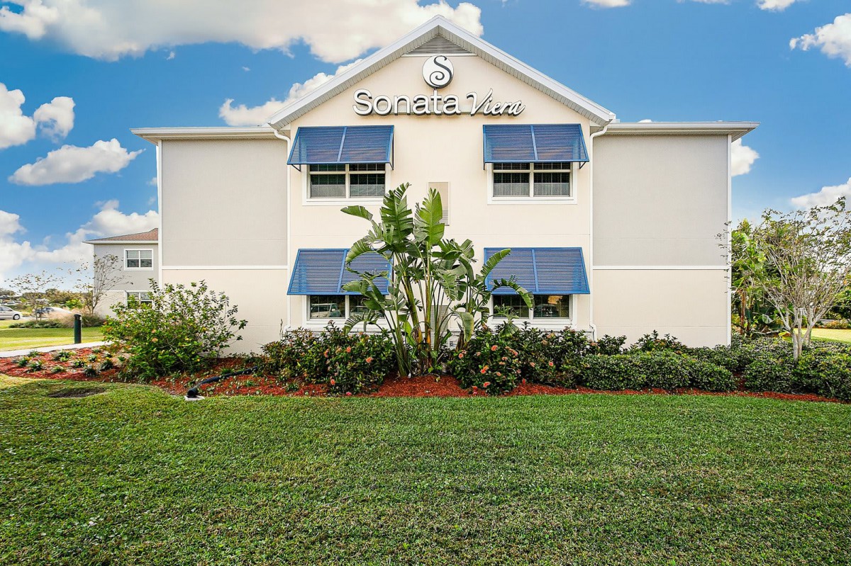 A well-maintained hotel building with a neatly landscaped lawn and blue awnings.