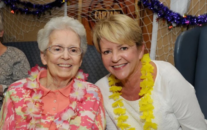 Two women smiling while wearing leis at a tropical-themed event.