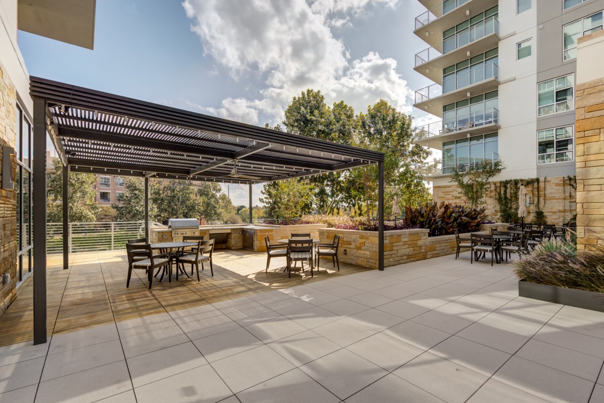 A modern outdoor patio with a pergola and seating area, set in an urban environment.