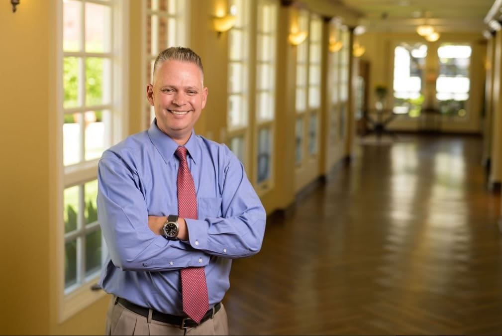 A man in business attire stands confidently in a well-lit hallway.