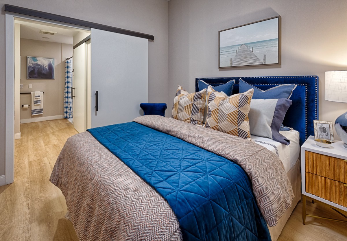 A modern bedroom featuring a neatly made bed with blue and beige accents, complemented by decorative pillows and a serene artwork on the wall.