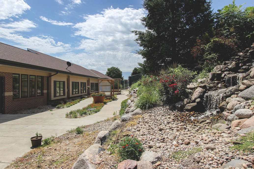 A building with a pathway surrounded by landscaped rocks and plants under a cloudy sky.