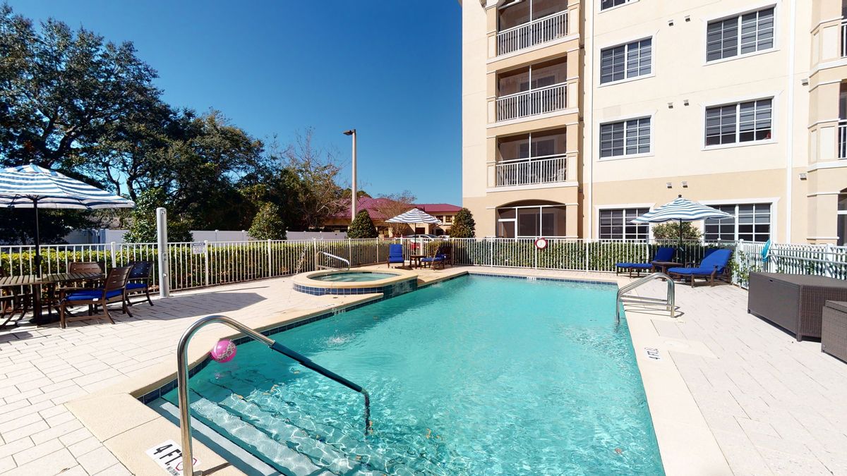 An outdoor swimming pool beside a multi-story apartment building on a sunny day.