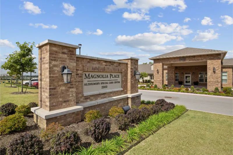 The entrance of Magnolia Place apartment complex, featuring a brick exterior and well-maintained landscaping.