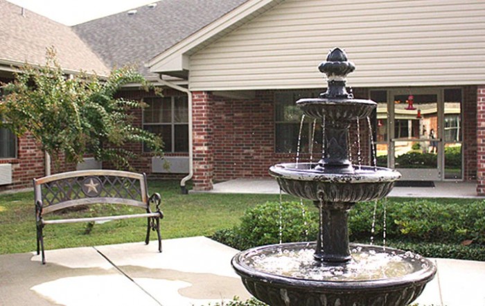 A tranquil garden scene featuring a multi-tiered fountain and a bench on a patio.