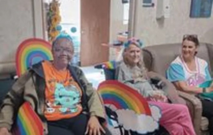 A group of people sitting together indoors, wearing colorful party hats and surrounded by rainbow decorations.