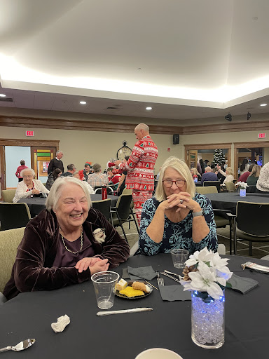 Two women enjoying a joyful moment at a social event with others in the background.