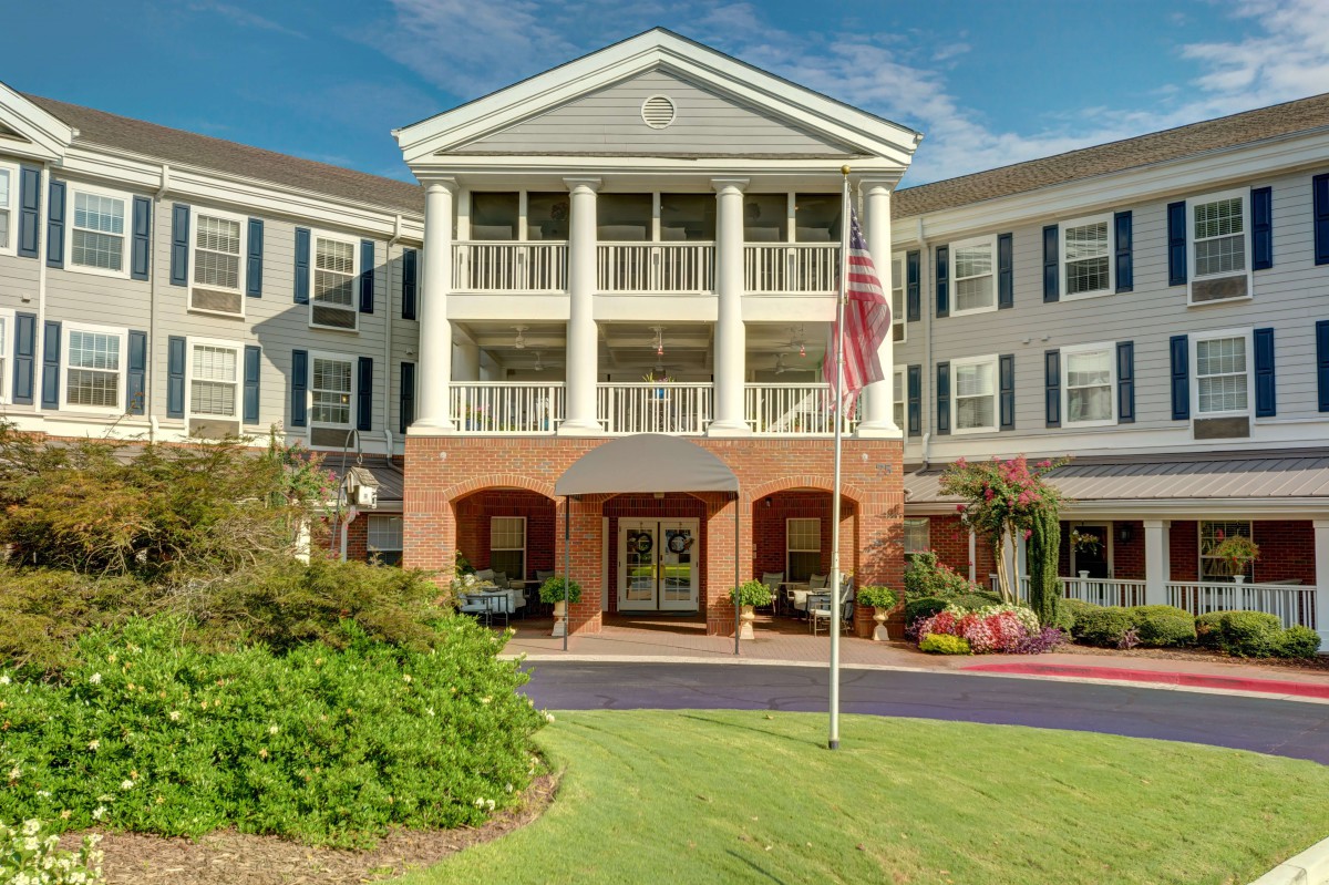 A large building with colonial-style architecture, featuring a front porch with columns and a neatly landscaped entrance.