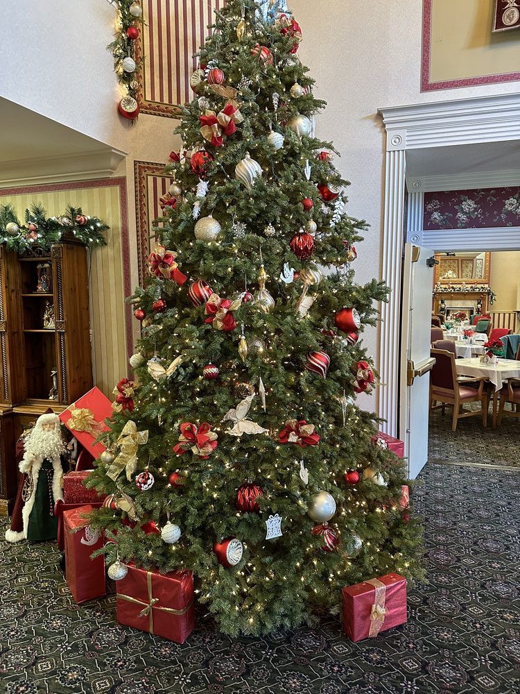 A beautifully decorated Christmas tree with red and white ornaments, surrounded by wrapped presents, stands indoors in a festive setting.