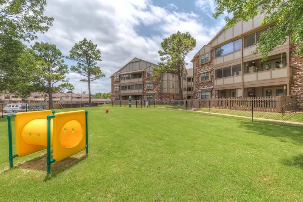 A residential apartment complex with a spacious green lawn and surrounding trees.