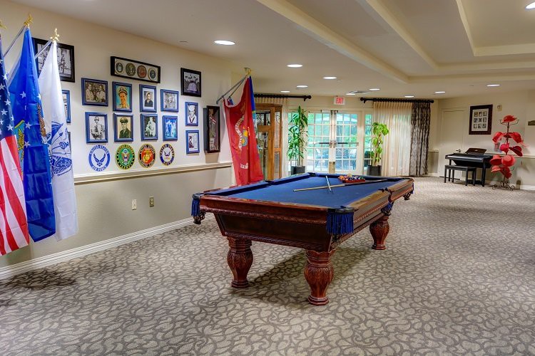 A well-decorated billiard room featuring a blue pool table surrounded by framed memorabilia and flags.